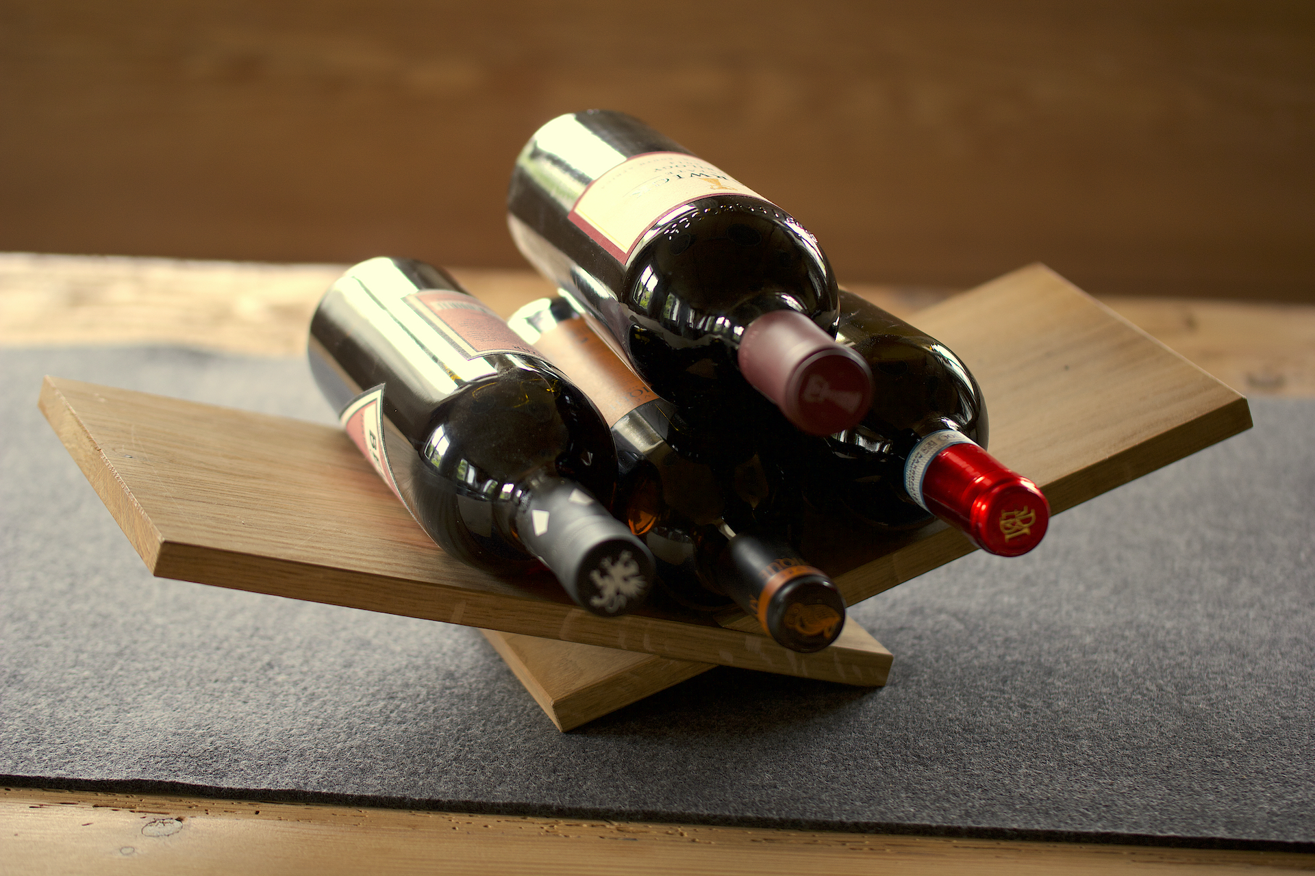 Eine Weinliege aus Holz auf einem Tisch, darauf 4 Flaschen Wein