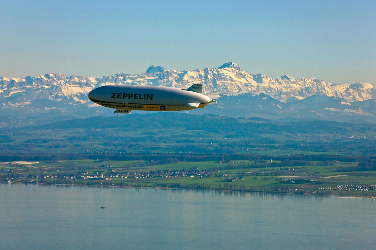 Ein Zeppelin schwebt in der Luft, im Hintergrund sind die Alpen